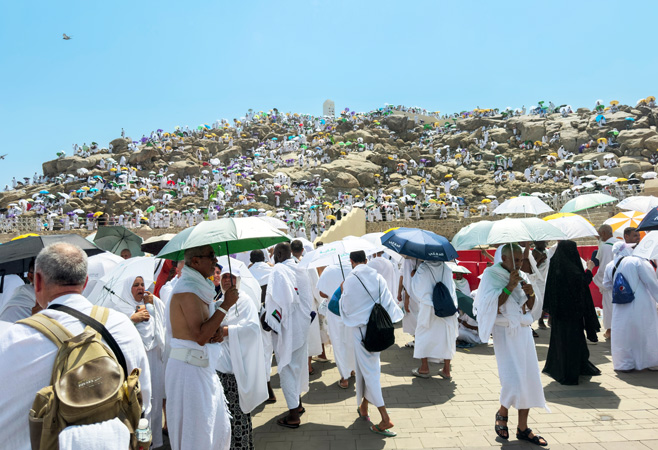 Pilgrims dressed in simple white ihram clothing walking toward Mount Arafat