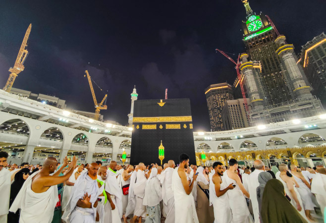 The majestic Clock Tower in Mecca illuminated against the night sky, surrounded by other buildings and skyscrapers.